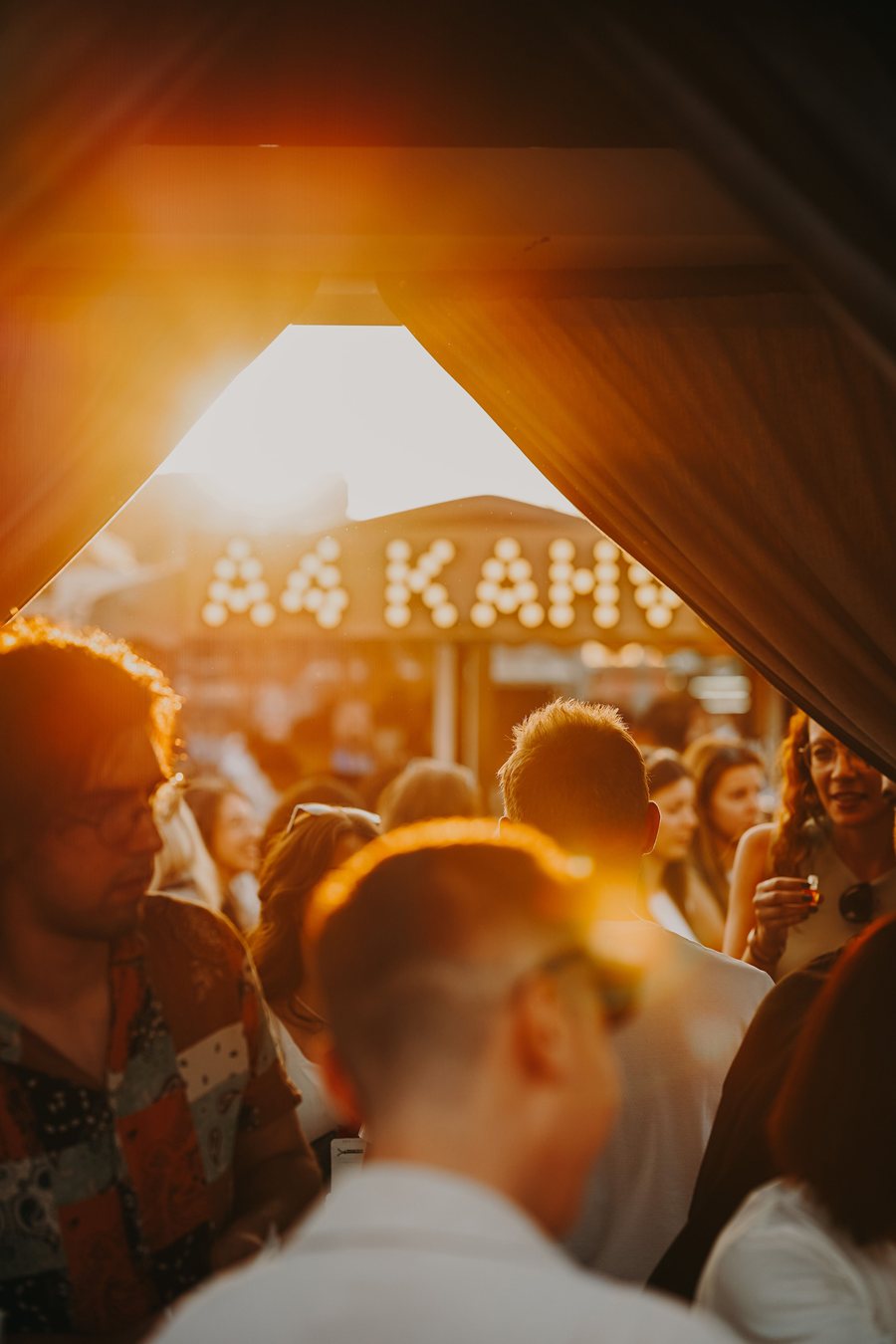 Golden hour through a tent, a crowd and a lit marquee.
