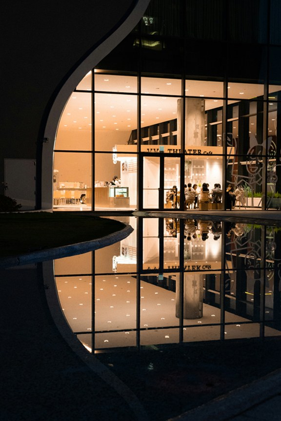 A night cafe behind glass, the room reflected in water.